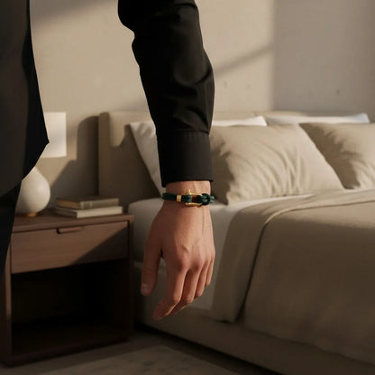 Homem usando pulseira masculina de corda verde com fecho dourado em um ambiente elegante de quarto.