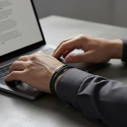 Homem trabalhando no notebook enquanto usa pulseira masculina de corda verde com volta dupla e fecho metálico prateado.