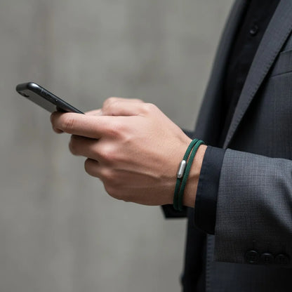 Homem usando celular enquanto veste pulseira masculina de corda verde com fecho metálico prateado.