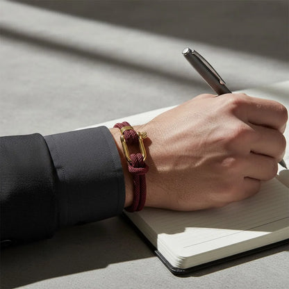 Homem escrevendo em um caderno enquanto usa pulseira masculina de corda vinho com fecho dourado.