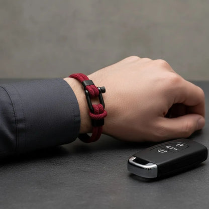 Pulso com pulseira masculina de corda vinho e fecho preto ao lado de chave de carro sobre a mesa.