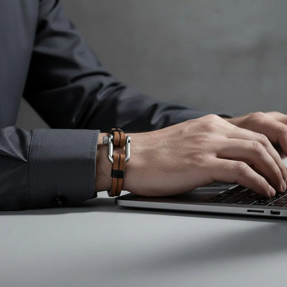 Pulseira masculina de couro marrom com fecho metálico prateado sendo usada enquanto a pessoa digita no notebook.