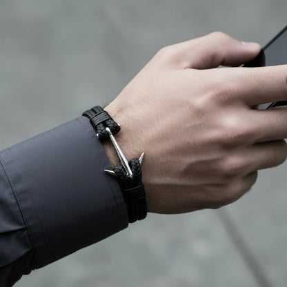 Homem usando celular enquanto veste pulseira masculina de couro trançado preto com detalhe de âncora prateada.