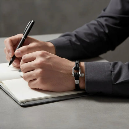 Homem escrevendo em um caderno e usando pulseira masculina de couro preto trançado com fecho prateado.