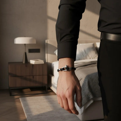 Homem usando pulseira masculina de couro preto trançado com fecho metálico em um quarto de hotel.