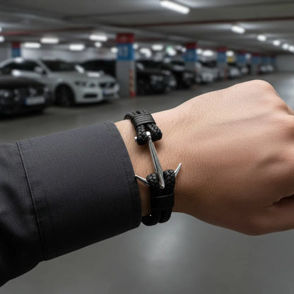 Homem usando pulseira masculina de couro trançado preto com detalhe de âncora metálica prateada em um estacionamento.