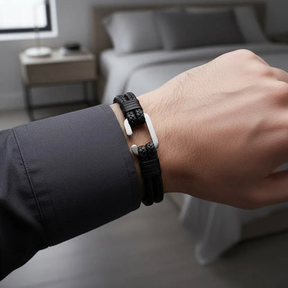 Close da pulseira masculina de couro trançado preto com detalhe metálico prateado no pulso em um quarto moderno.