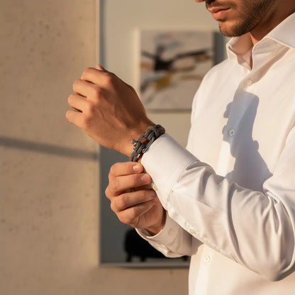 Homem ajustando a camisa social e usando pulseira masculina de corda cinza com fecho metálico.