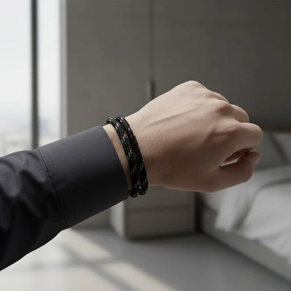Pulseira masculina de corda preta com pontos brancos e fecho cilíndrico preto em destaque no pulso.
