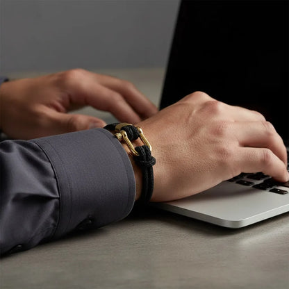 Homem trabalhando no notebook enquanto usa pulseira masculina de corda preta com fecho dourado.