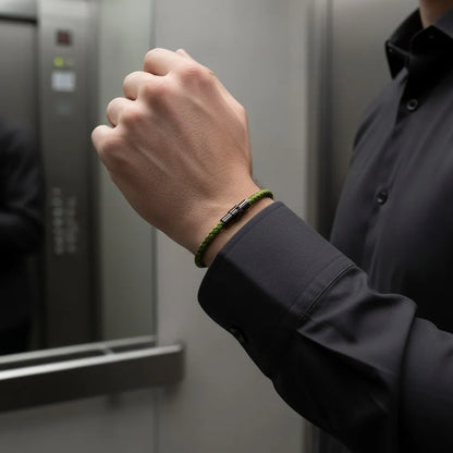 Close da pulseira masculina de corda verde trançada com fecho metálico preto em ambiente corporativo.