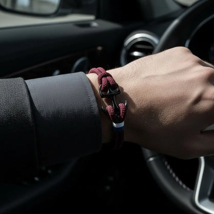 Pulseira masculina vinho de corda com fecho de âncora preta e acabamento tricolor, usada no pulso dentro de um carro.